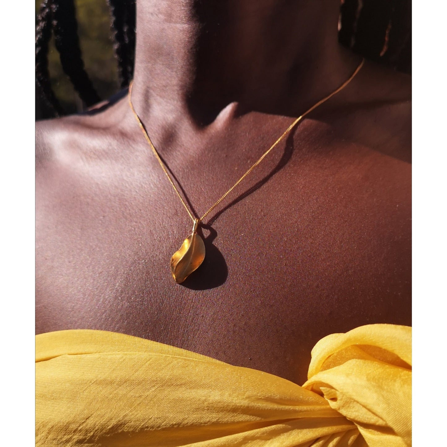 Sunkissed dark skin black woman wearing a bright yellow silk wrap and a large Fula pendant on a curb chain by ROKUS London.