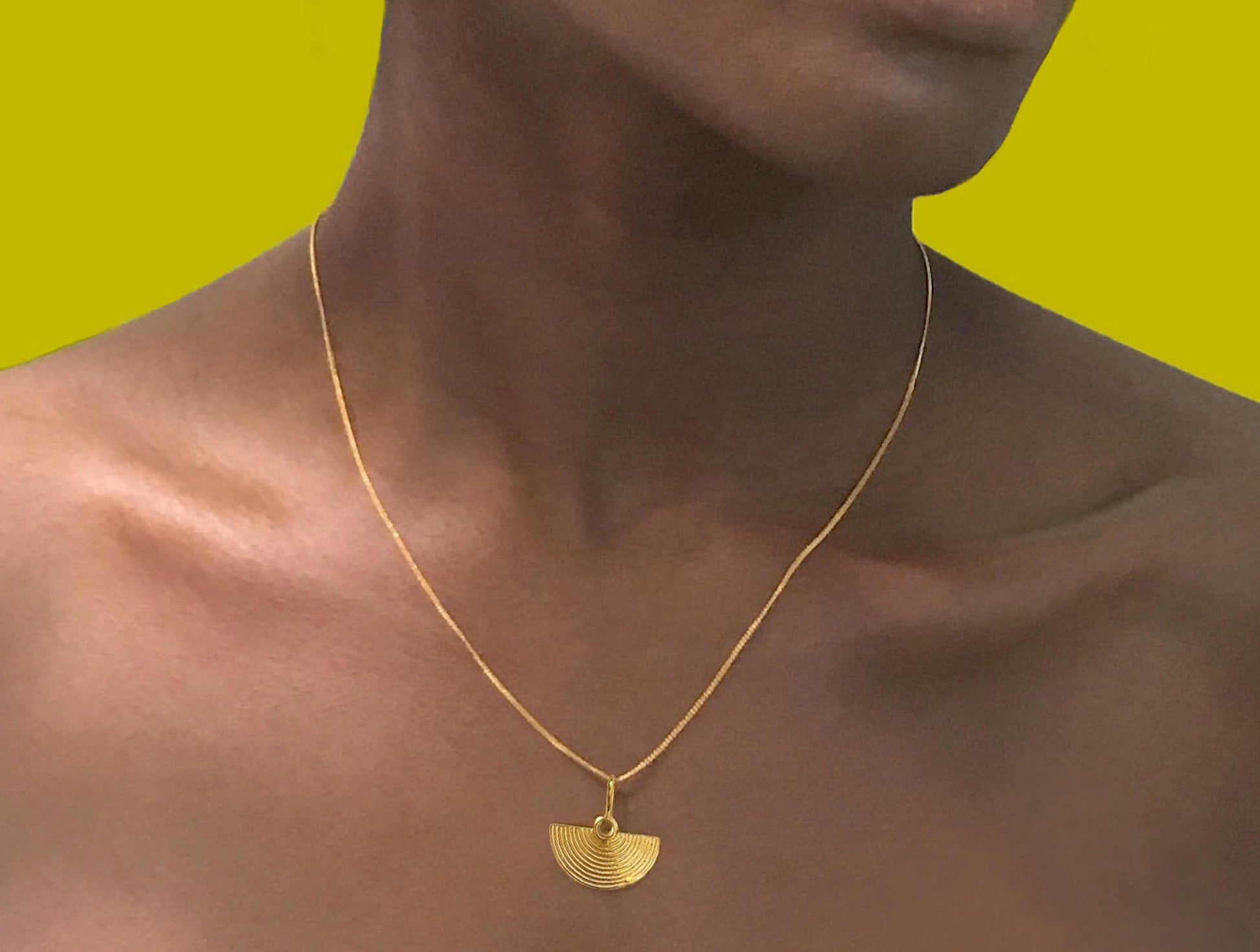 Half moon shaped texture pendant on a fine curb chain made by ROKUS and worn by a woman with a glowing black skin and a lime green background. 